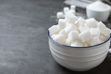 Photo of Refined sugar cubes in bowl on grey table. Space for text