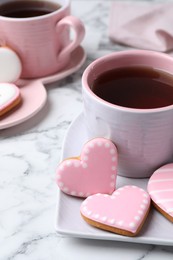 Photo of Delicious heart shaped cookies and cup of tea on white marble table, closeup