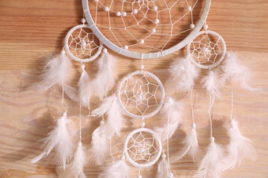 Photo of Beautiful dream catcher hanging on wooden wall, closeup
