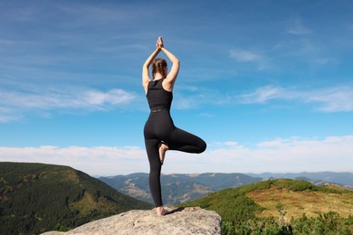 Young woman practicing outdoor yoga in mountains, back view. Fitness lifestyle