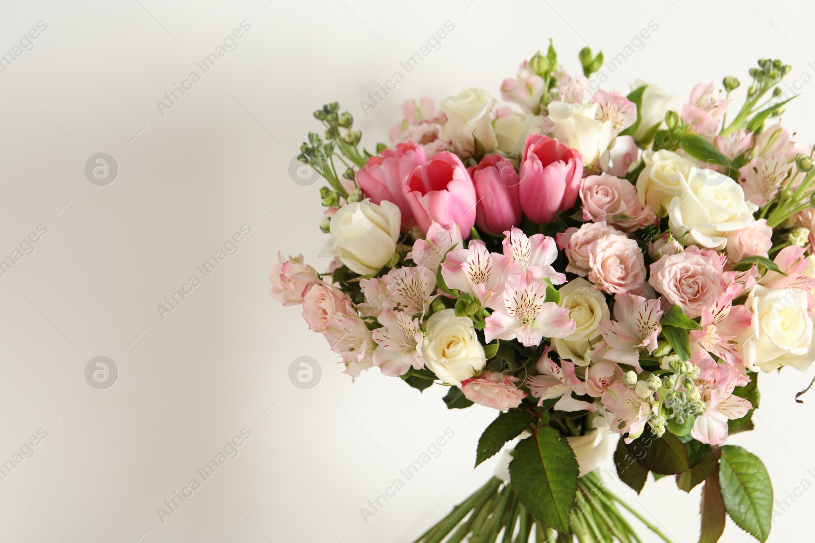 Photo of Beautiful bouquet of fresh flowers near white wall, space for text