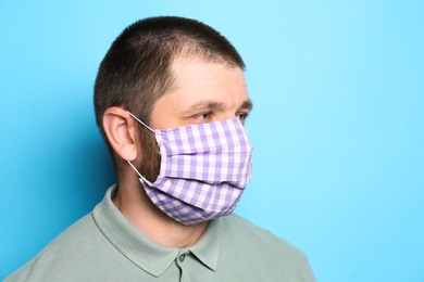 Photo of Man wearing handmade cloth mask on light blue background, space for text. Personal protective equipment during COVID-19 pandemic
