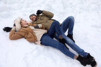Photo of Happy couple lying on snow outdoors. Winter vacation