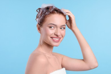 Happy young woman washing her hair with shampoo on light blue background