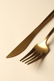 Stylish golden cutlery. Fork and knife on beige background