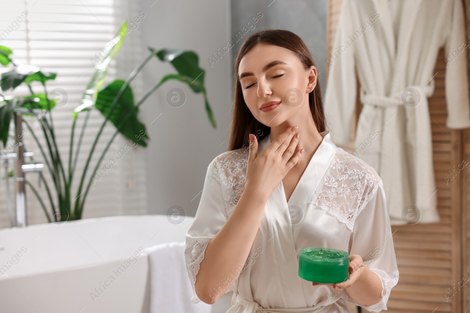 Photo of Young woman applying aloe gel onto her neck in bathroom