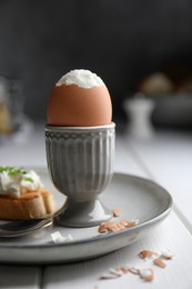 Fresh soft boiled egg in cup and sandwich on white wooden table