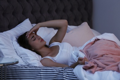 Photo of Young woman suffering from headache while lying in bed at night. Sleeping problems