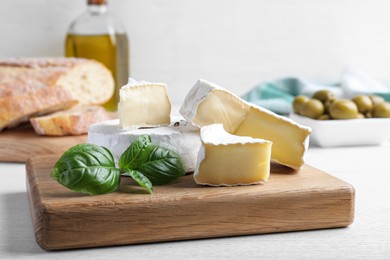 Photo of Tasty brie cheese with basil on white wooden table