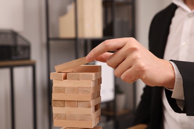 Photo of Playing Jenga. Man building tower with wooden blocks indoors, closeup