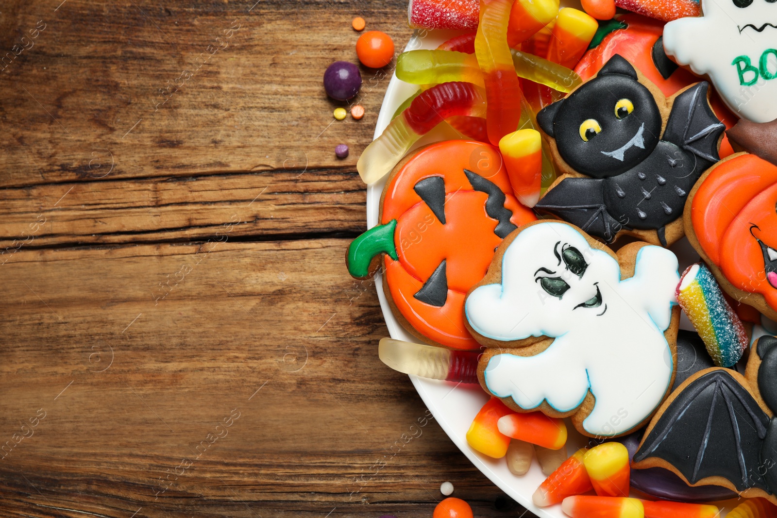 Photo of Tasty cookies and sweets for Halloween party on wooden table, top view. Space for text