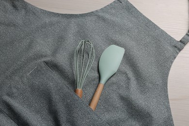 Stylish apron, spatula and whisk on white wooden table, top view