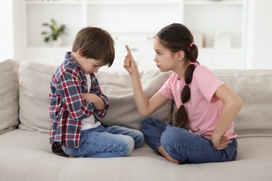 Photo of Upset brother and sister having argument on sofa at home