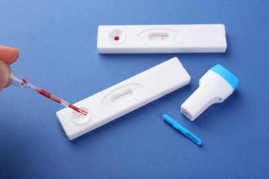 Photo of Woman dropping blood sample onto disposable express test cassette with pipette on blue background, closeup