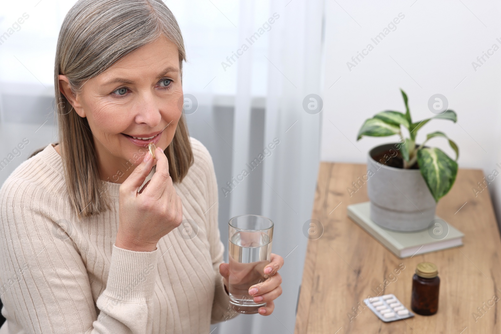 Photo of Beautiful woman taking vitamin pill at table indoors