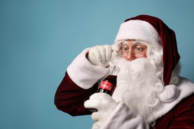 MYKOLAIV, UKRAINE - JANUARY 18, 2021: Santa Claus holding Coca-Cola bottle on light blue background