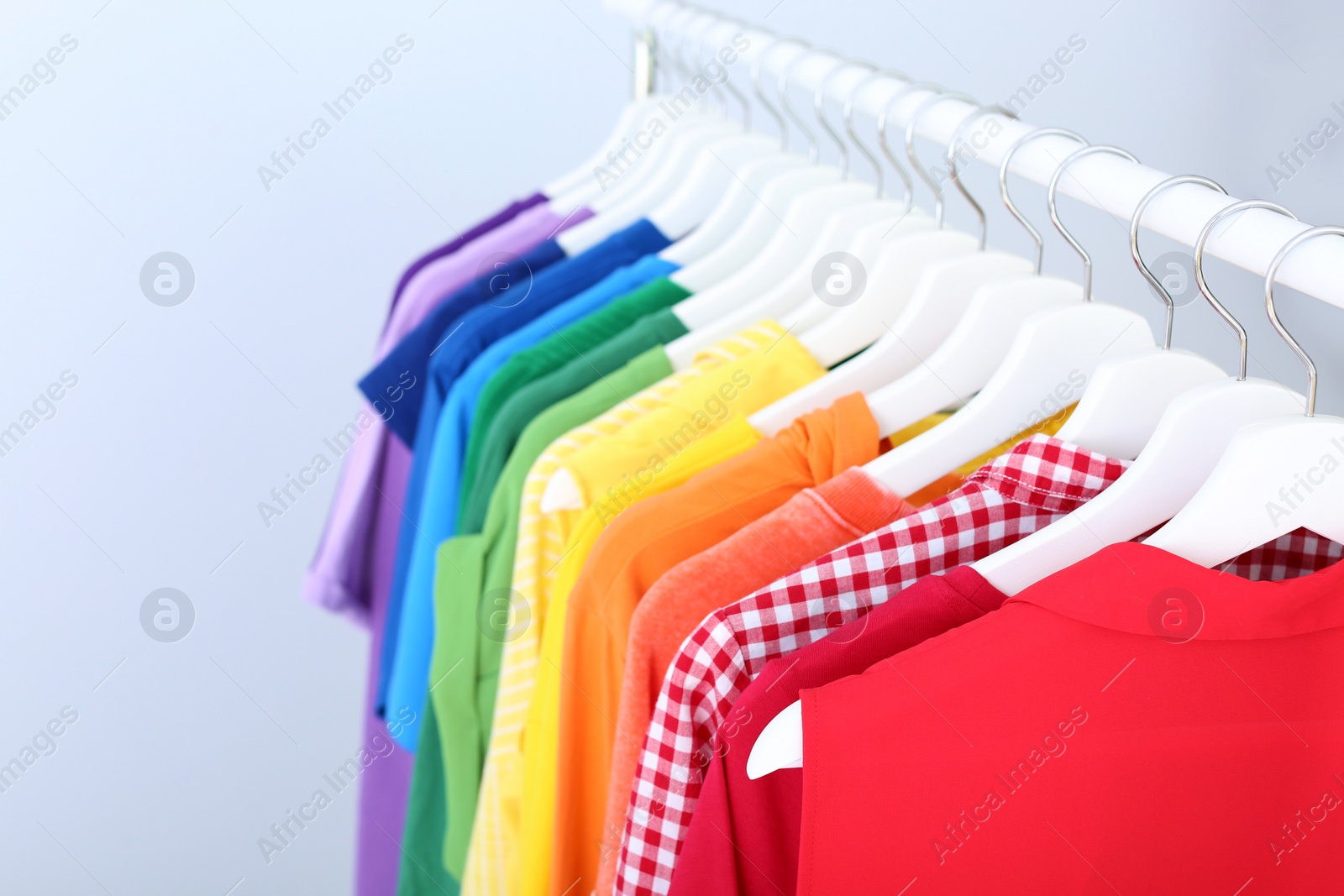 Photo of Rack with rainbow clothes on light background