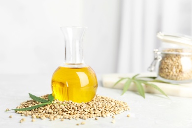 Bottle with hemp oil, leaf and seeds on white table