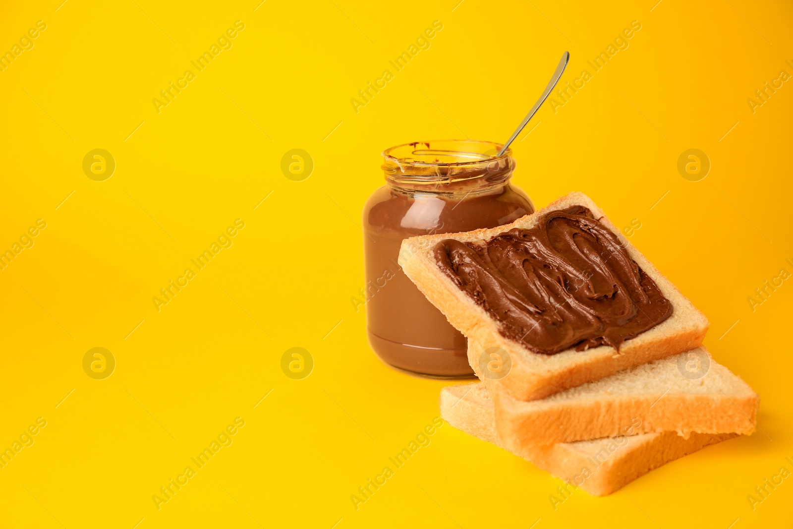 Photo of Tasty toast with chocolate paste and jar of cream on yellow background, space for text