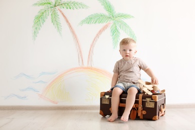 Photo of Adorable little child playing traveler with suitcase indoors