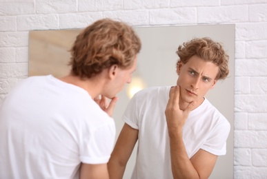 Photo of Young man looking in mirror after shaving at home