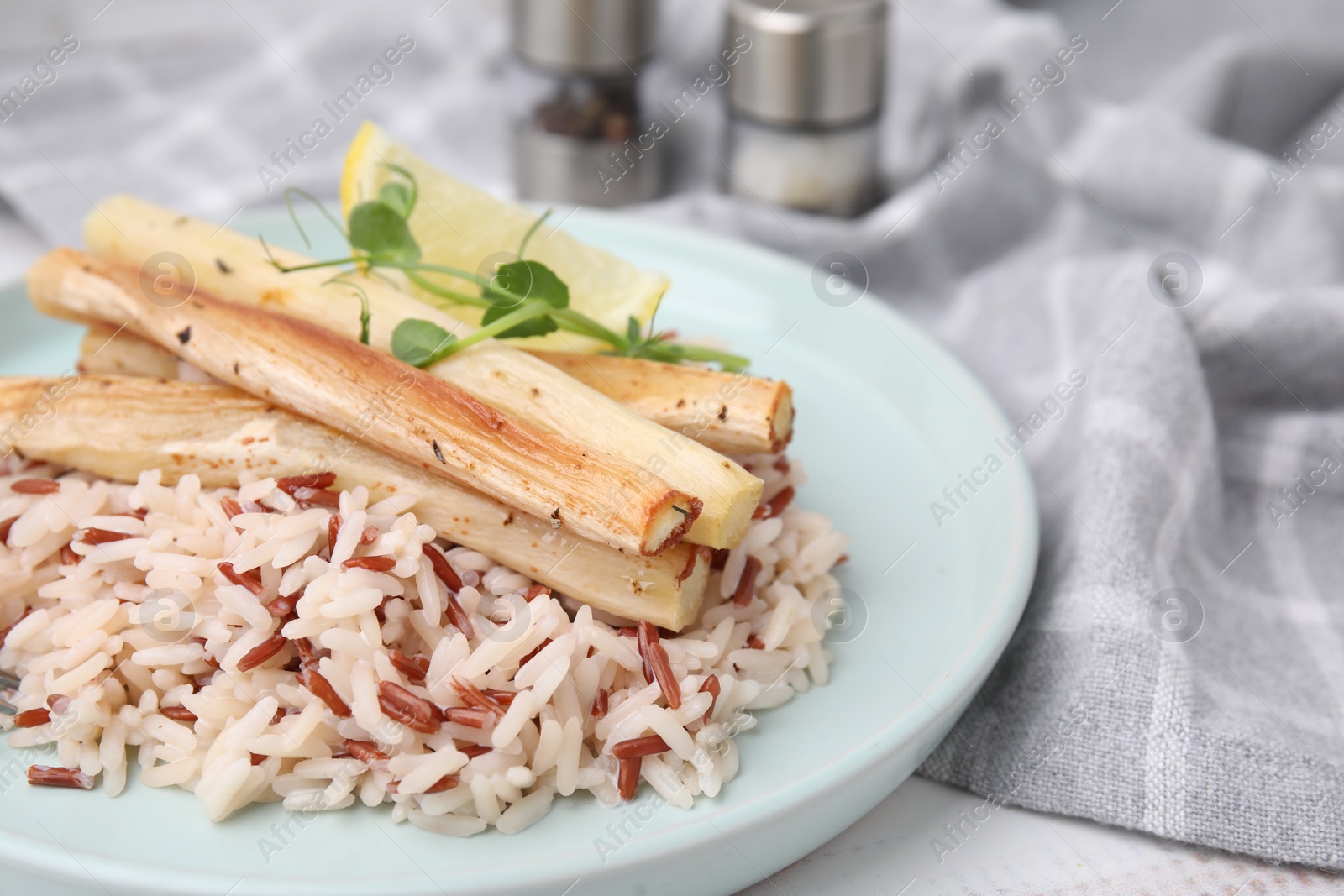 Photo of Plate with baked salsify roots, lemon and rice on table, closeup