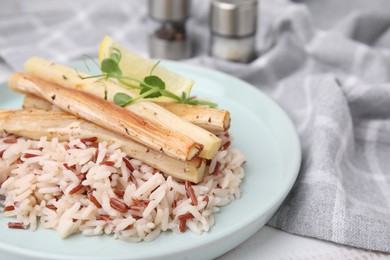Plate with baked salsify roots, lemon and rice on table, closeup