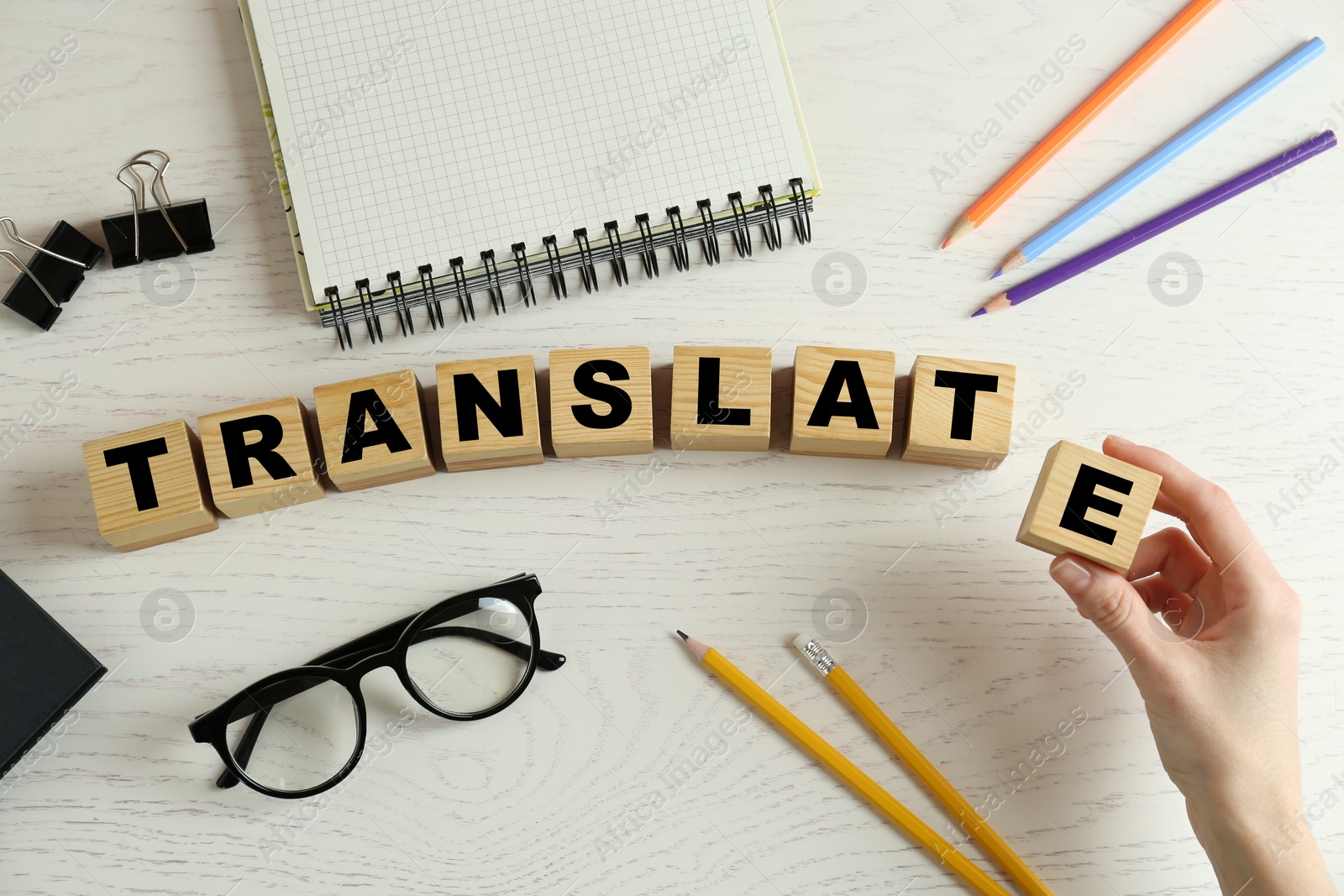 Photo of Woman making word Translate with wooden cubes at white table, top view