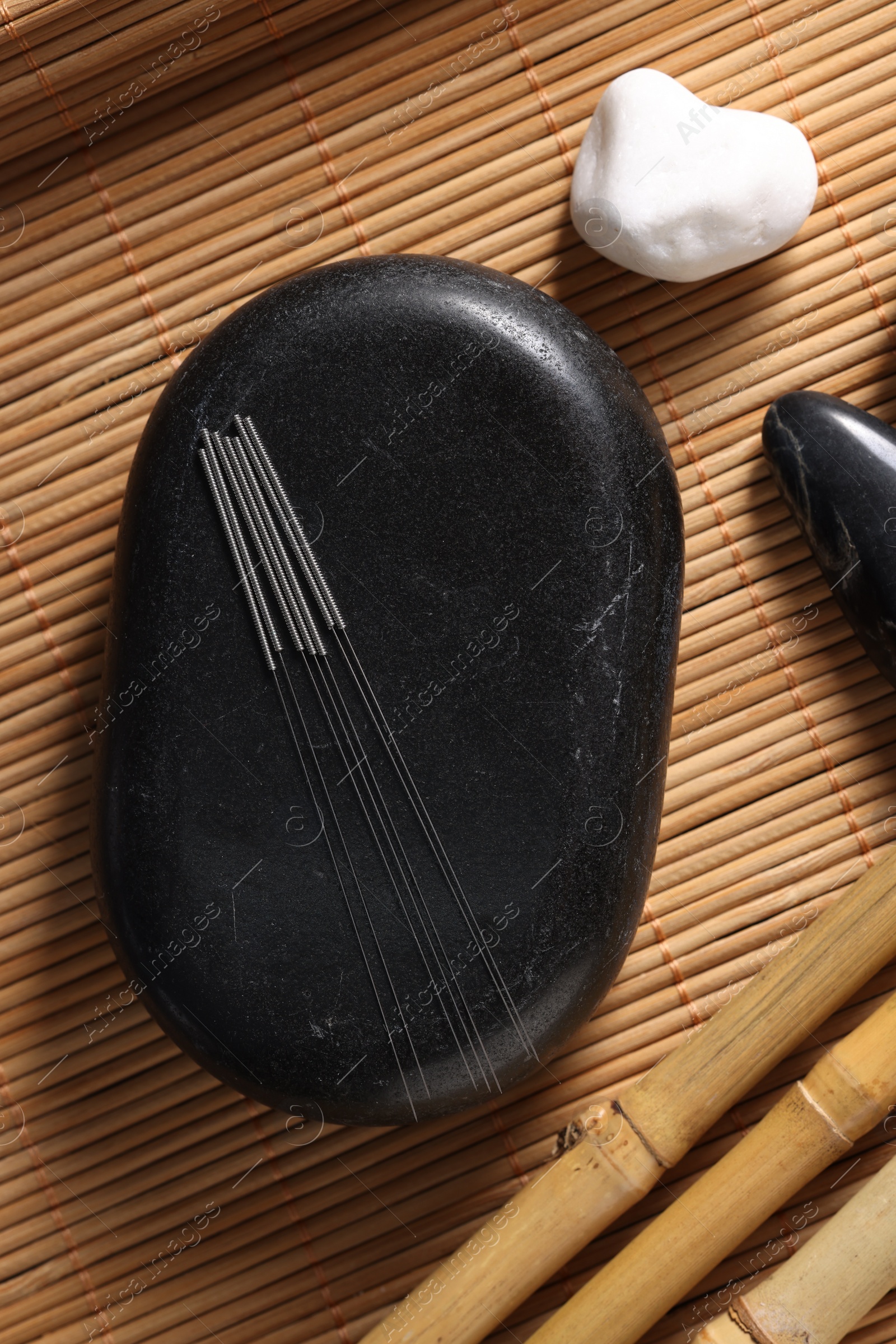 Photo of Stones with acupuncture needles on bamboo mat, flat lay