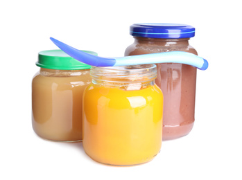 Jars with baby food and spoon on white background