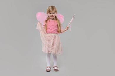 Cute little girl in fairy costume with pink wings and magic wand on light grey background