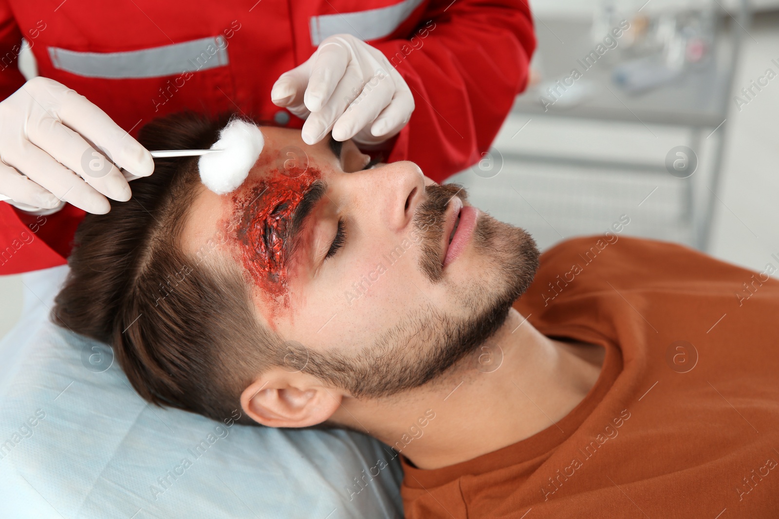 Photo of Nurse cleaning young man's head injury in clinic. First aid