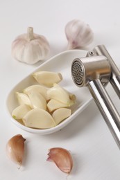 Metal press and garlic on white wooden table, closeup