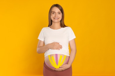 Photo of Pregnant woman with kinesio tapes on her belly against orange background