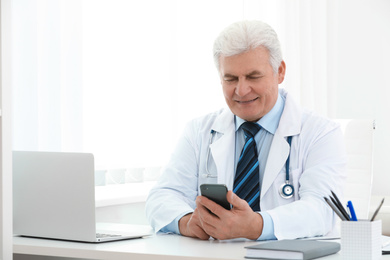 Photo of Senior doctor with smartphone at table in office