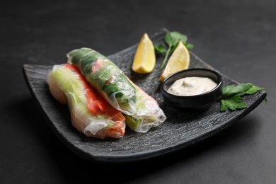 Photo of Delicious rolls wrapped in rice paper served on black table, closeup