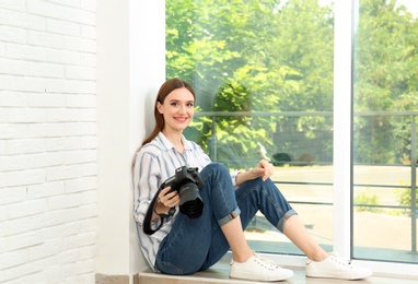 Professional photographer with modern camera sitting near window indoors