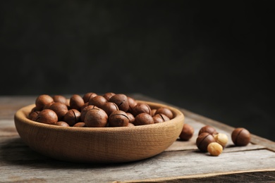 Photo of Plate with organic Macadamia nuts on table against dark background. Space for text