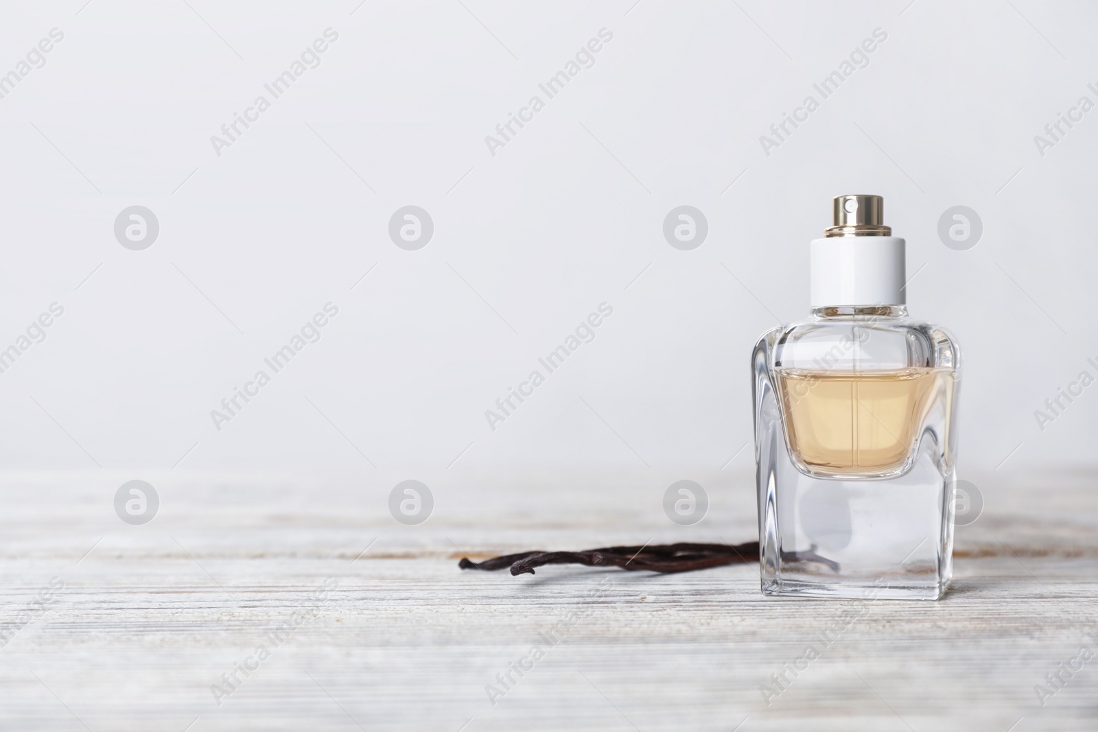 Photo of Perfume bottle and vanilla pods on wooden table against light background