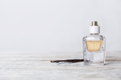 Photo of Perfume bottle and vanilla pods on wooden table against light background