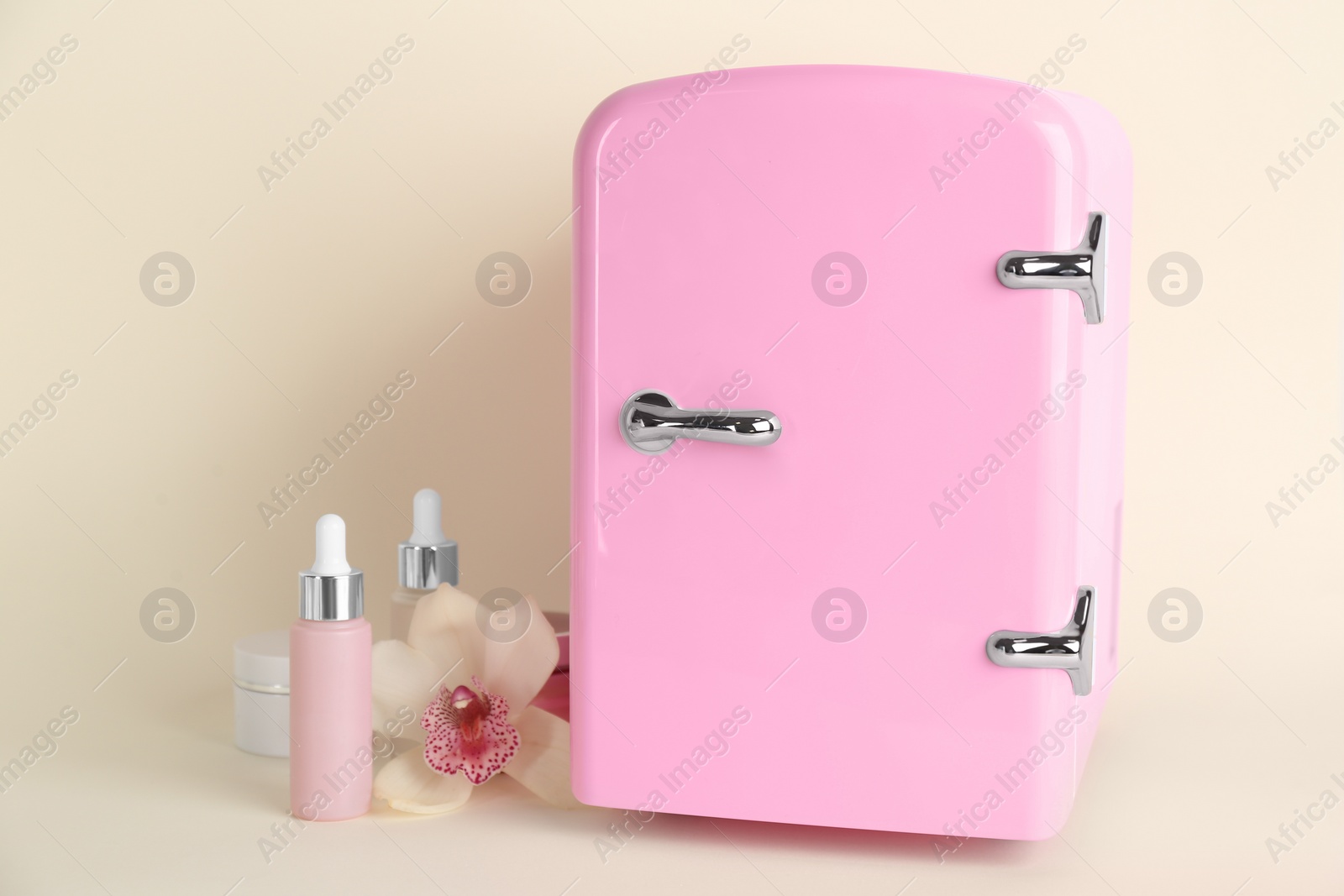 Photo of Cosmetic refrigerator and skin care products on beige background