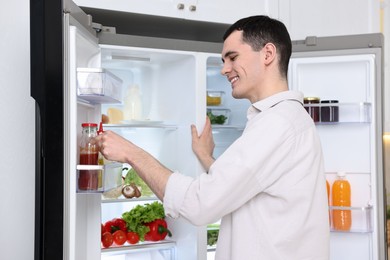 Happy man near refrigerator in kitchen at home