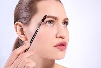 Photo of Beautiful woman with perfect eyebrows applying makeup on light background