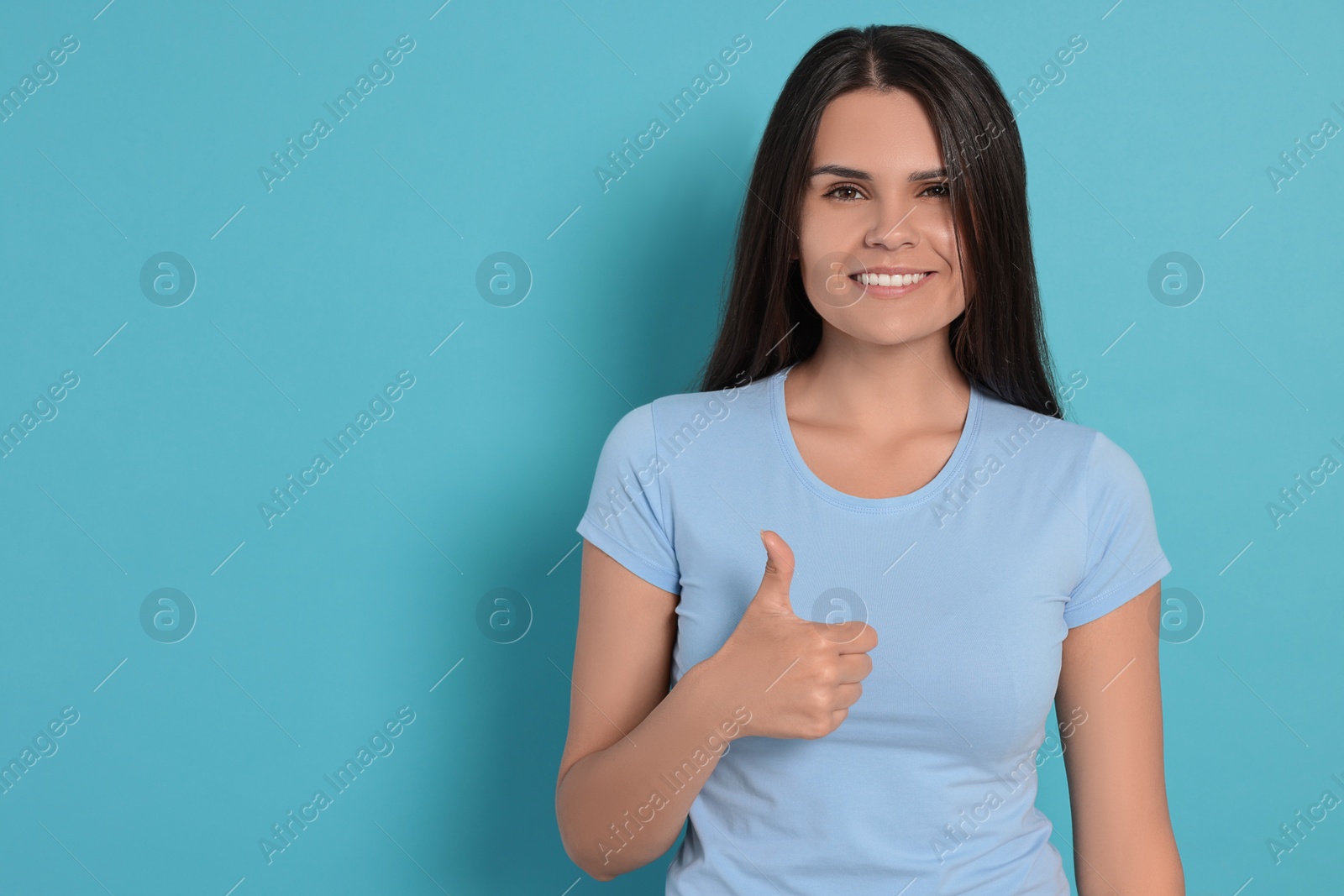 Photo of Young woman showing thumb up on light blue background, space for text