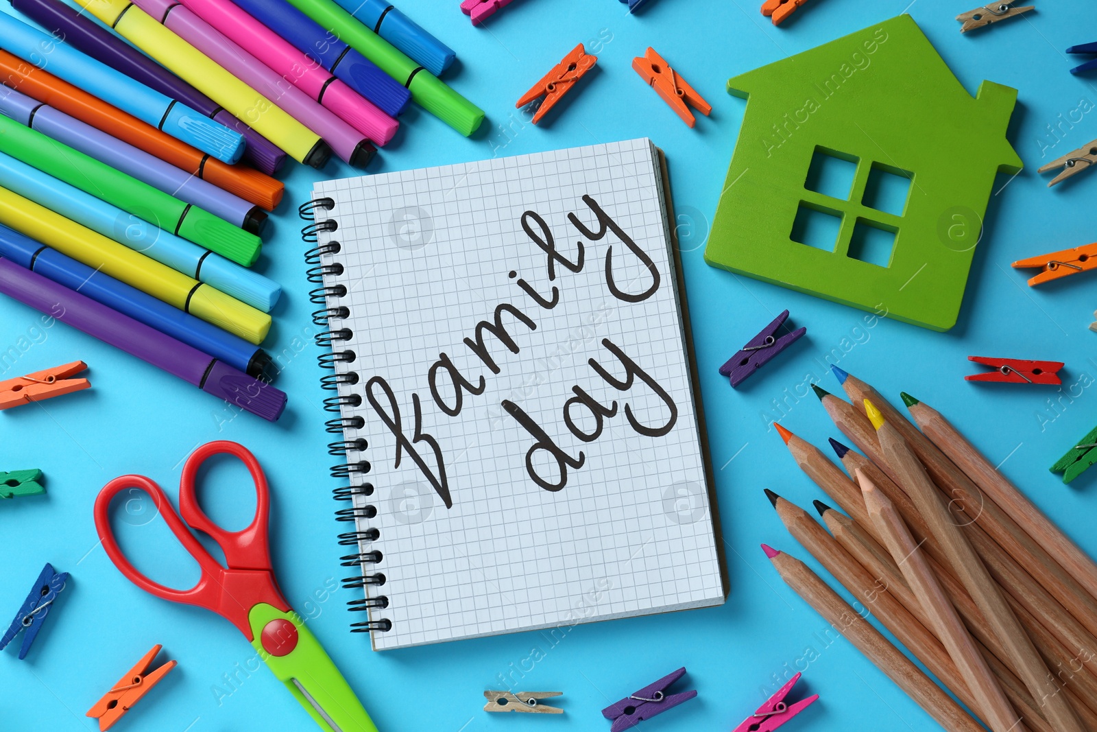 Photo of Happy International Family Day. Flat lay composition with notebook and stationery on light blue background