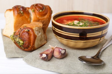 Photo of Delicious borsch served with pampushky on white wooden table, closeup. Traditional Ukrainian cuisine