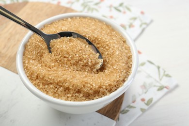 Photo of Brown sugar in bowl and spoon on table, closeup