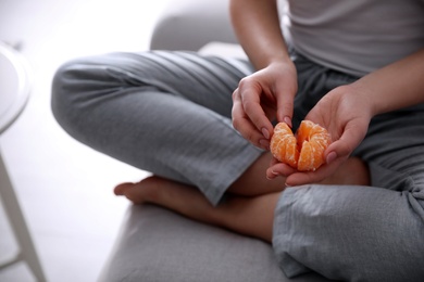 Young woman with peeled ripe tangerine on sofa indoors, closeup