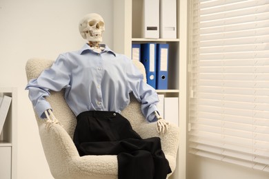 Waiting concept. Human skeleton sitting in armchair at office