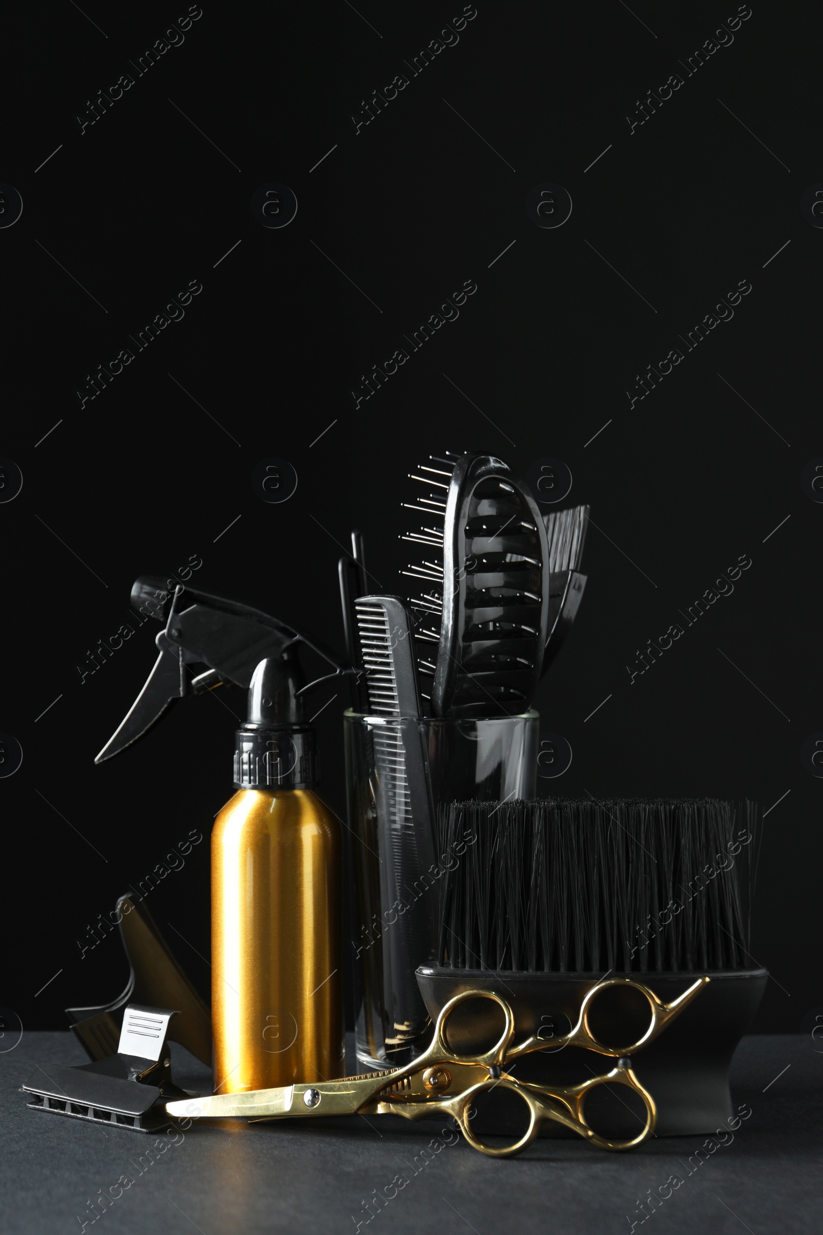 Photo of Different hairdresser tools on grey table against black background